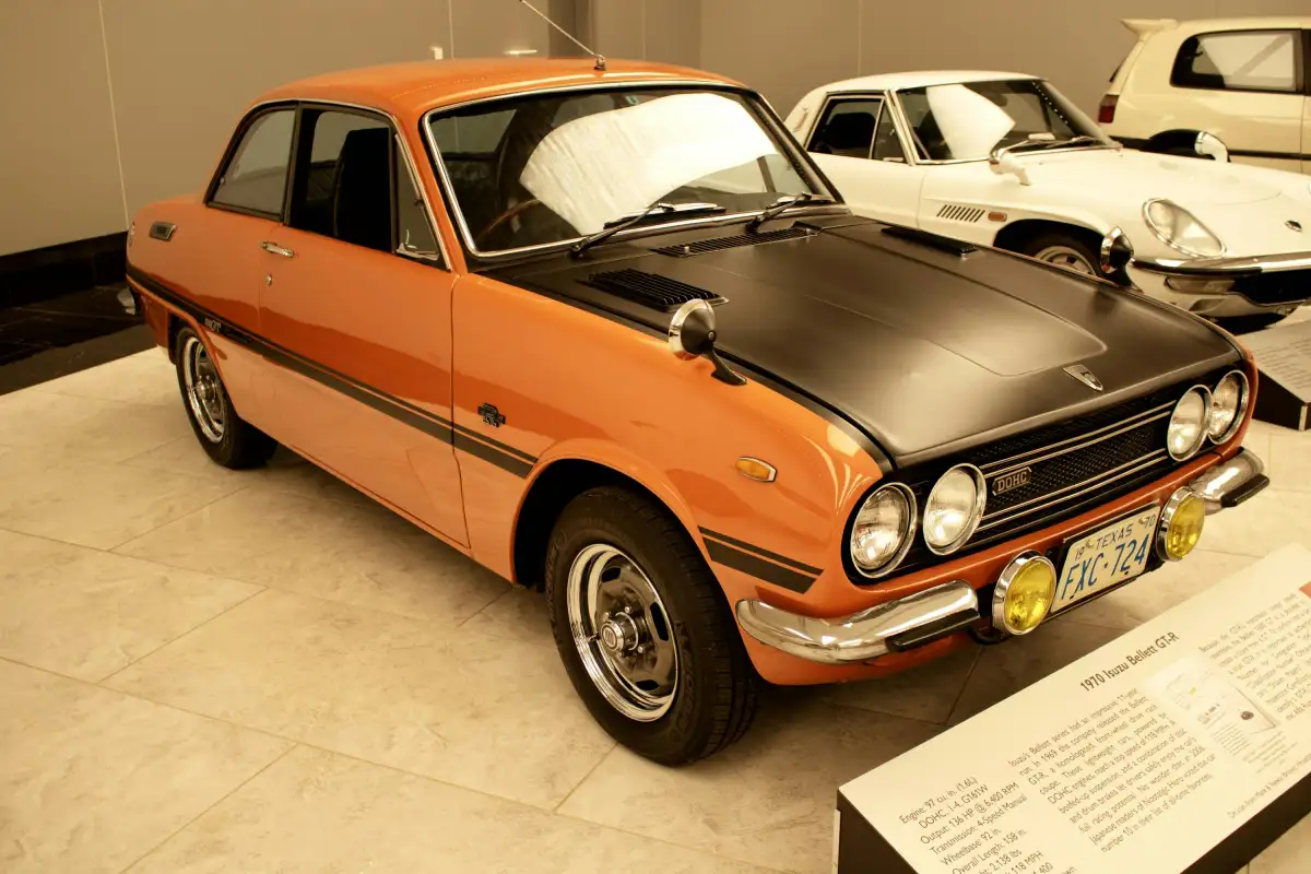 A vintage orange car is parked in a museum.